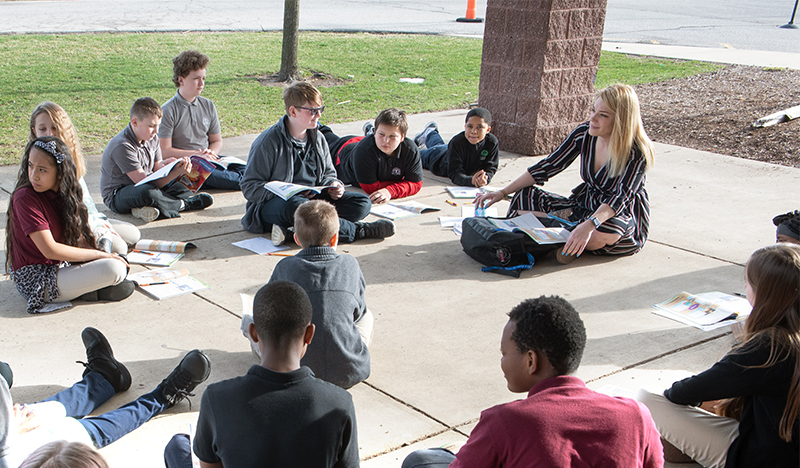 Teacher at Trillium Academy sitting in circle with students during an outdoor lesson.