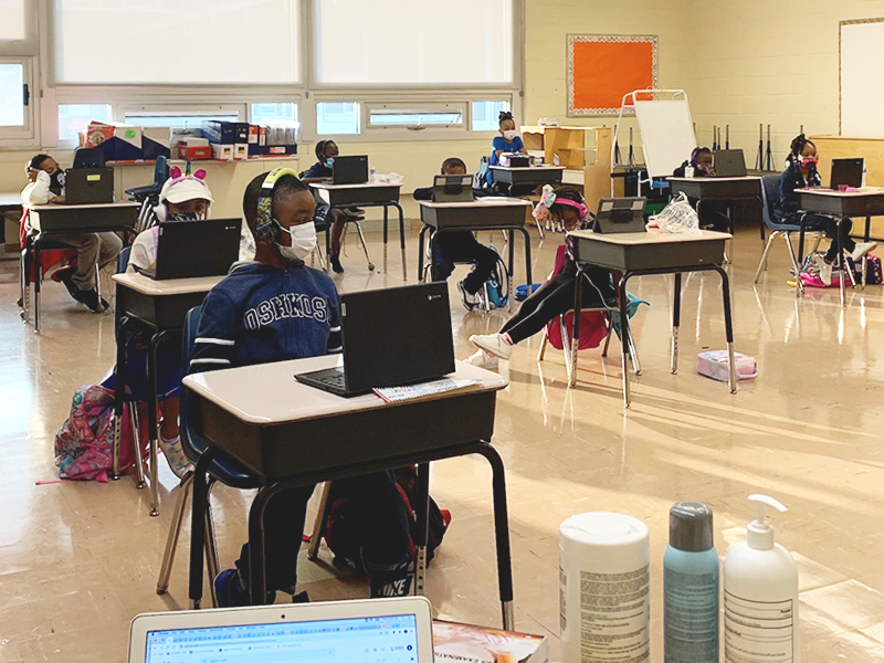 Students at Distinctive College Prep sitting at their desks in their classroom, wearing masks, and working on their laptop computers.