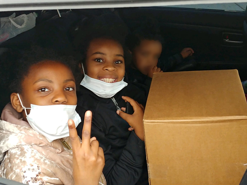 Two students from International Academy of Flint sitting in car with masks, picking up supplies at the school.