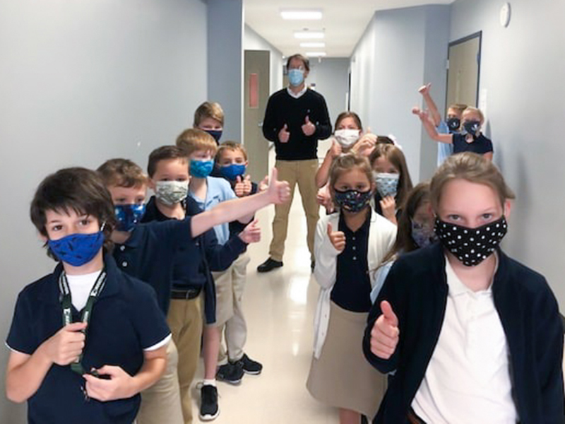 Students and teacher from Ivywood Classical Academy lined up in a hallway. Everyone is holding their thumbs up and wearing masks.