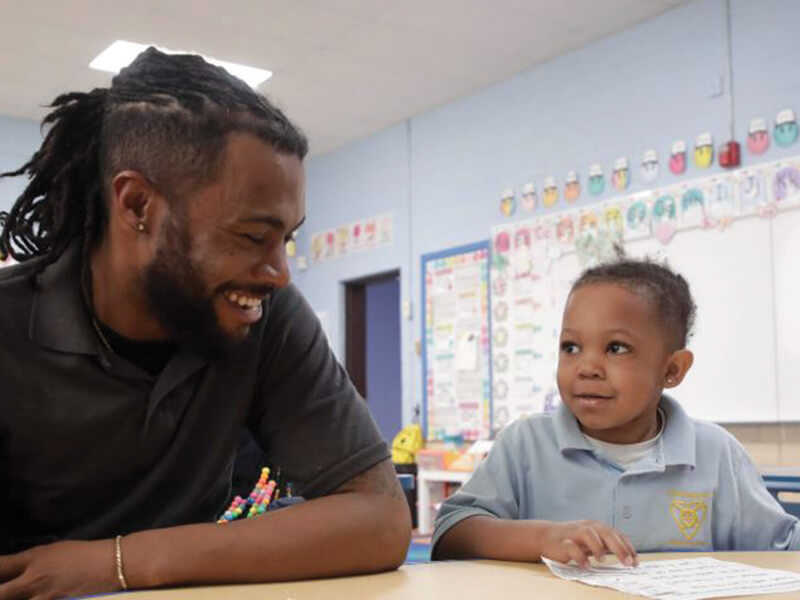 Teacher sitting with young student. Teacher and student are smiling at each other.