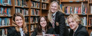 Four students smiling at the camera in the library of Charyl Stockwell Preparatory Academy High School.
