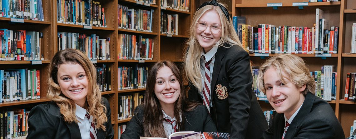 Four students smiling at the camera in the library of Charyl Stockwell Preparatory Academy High School.