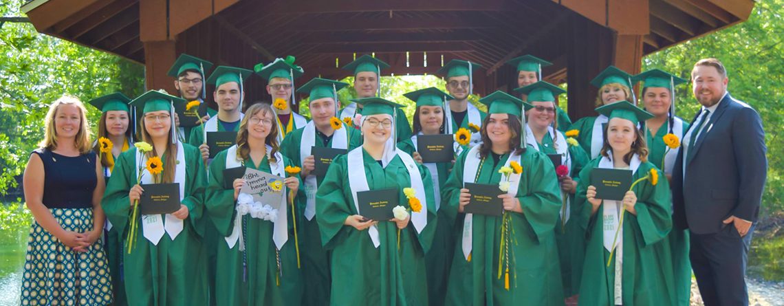 2021 Graduating class and administrators from Pansophia Academy standing outdoors in front of a covered bridge.